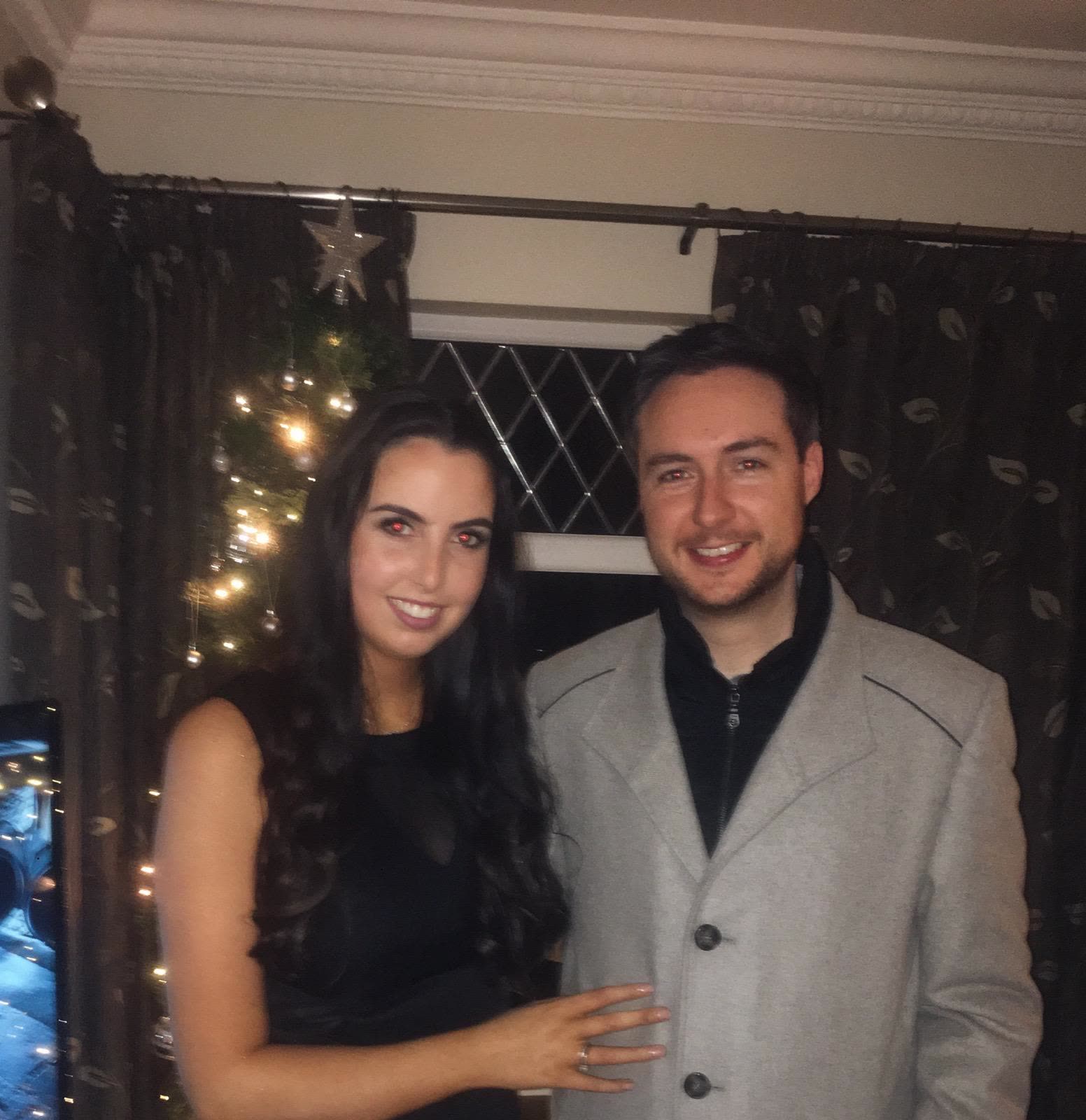 Showing off the engagement ring beside the Christmas tree