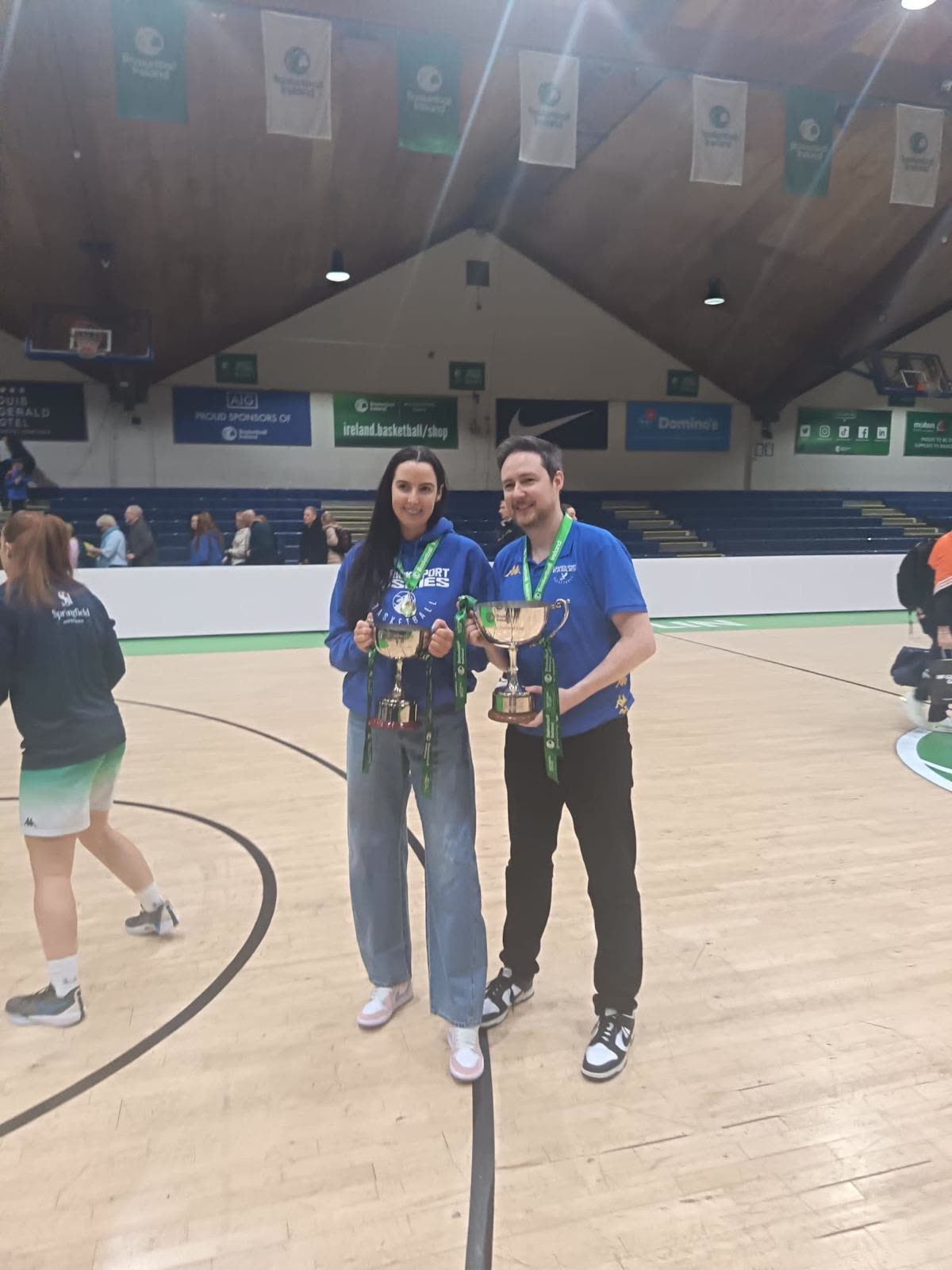Orlaith and Niall on a basketball court, each holding a trophy cup