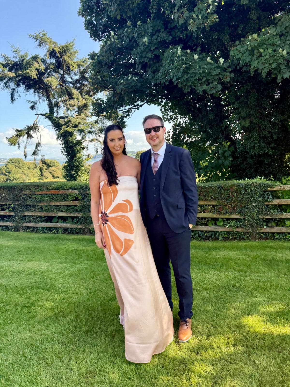 Dressed for a wedding on a green lawn with tall trees behind